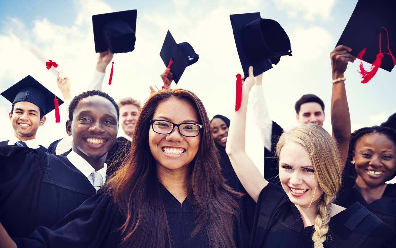 Group of diverse graduates celebrating with caps in the air.